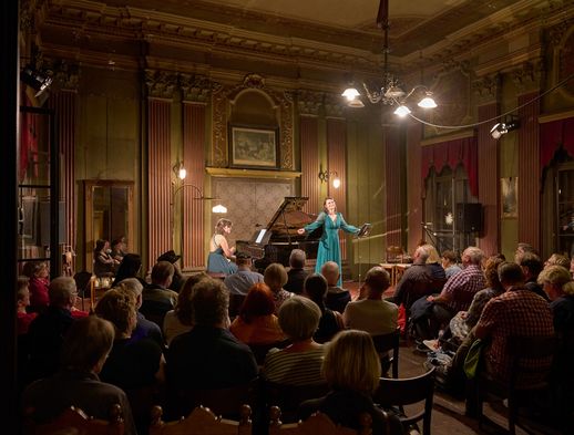 Eine Sängerin und eine Pianistin treten vor Publikum im festlich beleuchteten Saal des Prinzenpalais auf.