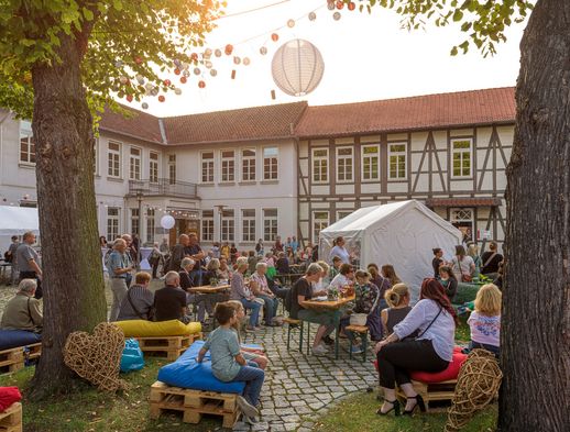 Menschen sitzen und stehen bei einem Kulturfest im Innenhof mit Fachwerkhäusern und Lichterketten.