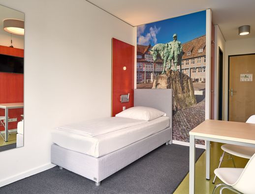 Modern eingerichtetes Einzelzimmer mit Bett, Schreibtisch, Wandbild und hellem Tageslicht.