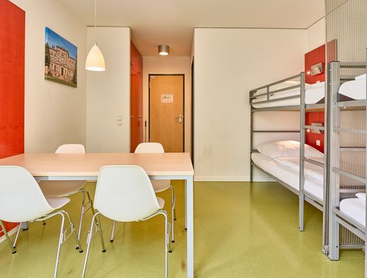 Helles Vierbettzimmer mit Etagenbetten, Tisch und Stühlen, modern eingerichtet in warmen Farben.