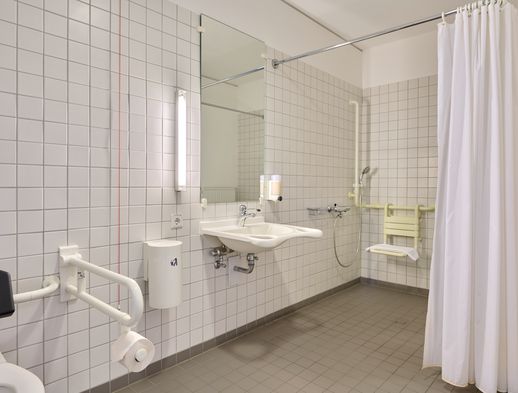Barrierefreies Bad mit Haltegriffen, bodengleicher Dusche, Duschsitz und unterfahrbarem Waschbecken.
