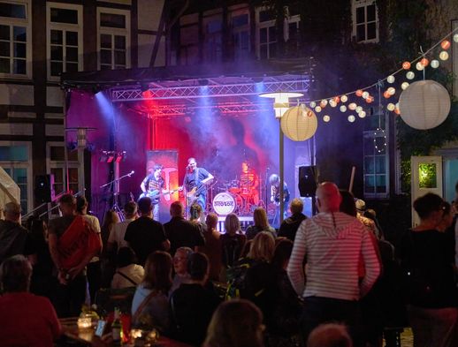 Open-Air-Konzert bei Nacht mit Band auf Bühne und Publikum unter Lichterketten.