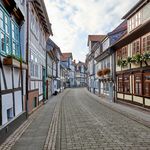Schmale Straße mit alten Fachwerkhäusern und Blumen an Fenstern.