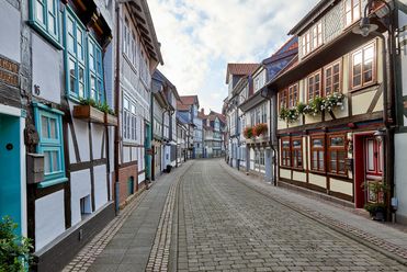 Schmale Straße mit alten Fachwerkhäusern und Blumen an Fenstern.