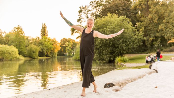 Eine lachende Frau balanciert barfuß auf einem Balken am Wasser