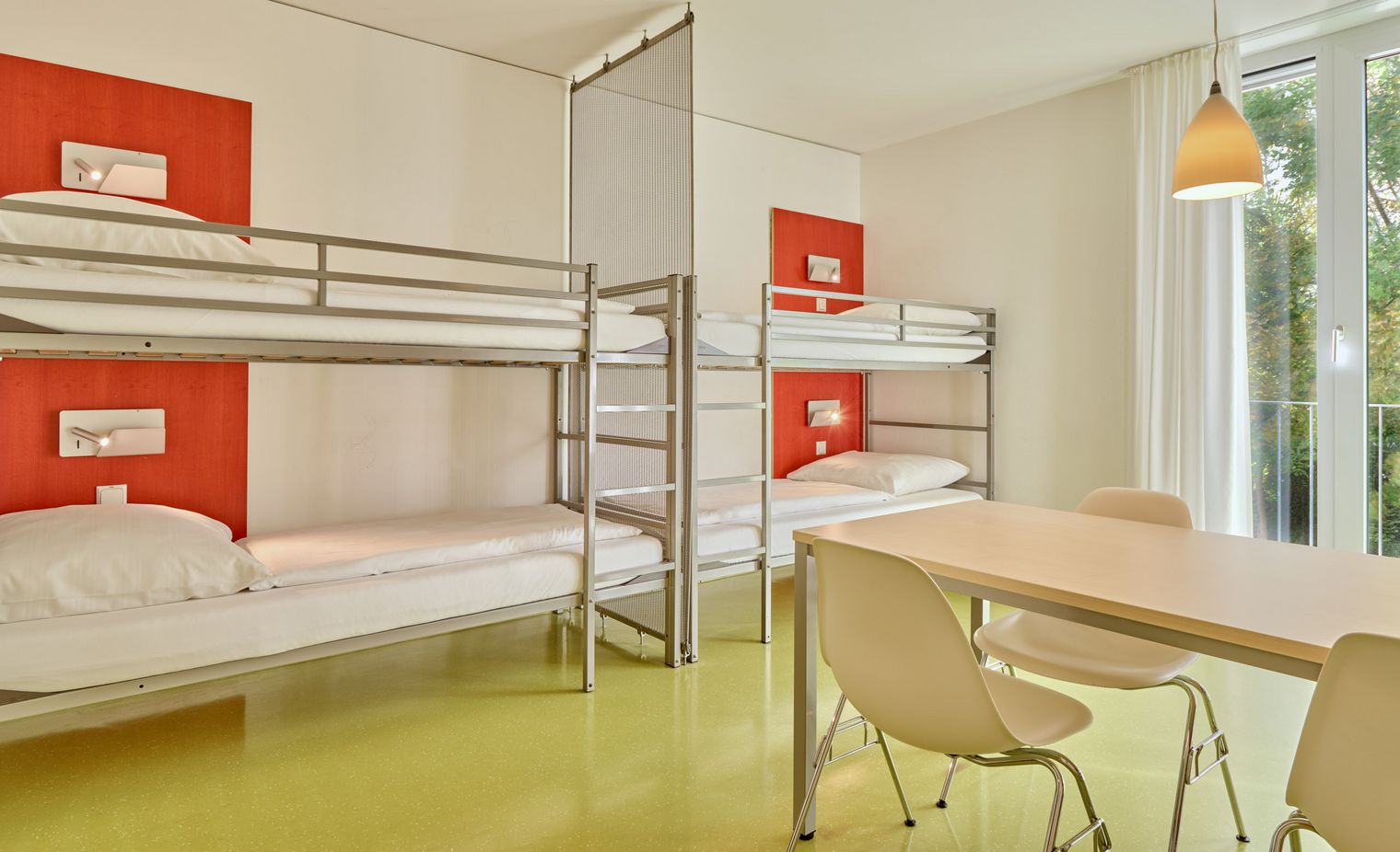 Helles Vierbettzimmer mit zwei Etagenbetten, Tisch, Stühlen und Fenster mit Blick ins Grüne