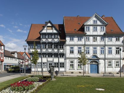 2 prächtige Fachwerkhäuser bei Sonnenschein stehen an einem Platz mit Wiese und einem Beet mit bunten Frühlingsblumen